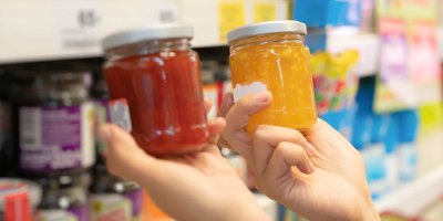 Ruce drží u regálu skleničky marmelády