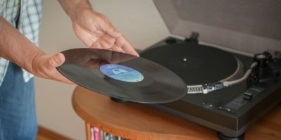 Muž drží vinylovou desku vedle gramofonu