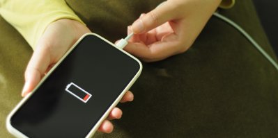 Žena drží v ruce telefon s vybitou baterií, připojuje k zařízení napájecí kabel