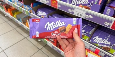 Ruka drží čokoládu Milku v obchodě oproti regálu