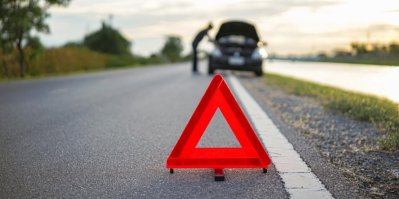 Výstražný trojúhleník na kraji silnice, v pozadí muž a auto