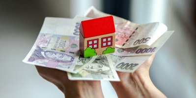 Ruce drží české bankovky a miniaturu domku