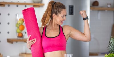 Mladá žena ve sportovním outfitu drží podložku na cvičení a ukazuje svaly na paži