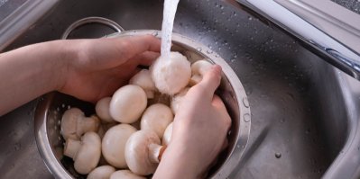 Žena umývá žampiony pod tekoucí vodou z kohoutku