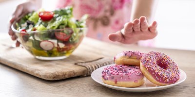 Roka odmítá donuty na bílém talíři, v pozadí je mísa se salátem