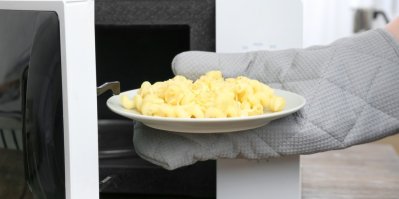 Člověk s kuchyňskou rukavicí vytahuje těstoviny na talíři z mikrovlnné trouby