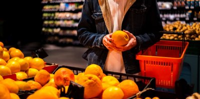 Člověk v obchodě vybírá pomeranč z hromady citrusů