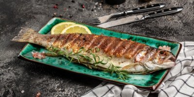 Grilovaný pstruh na obdélníkovém talíři se snítkou rozmarýnu a plátky citronu