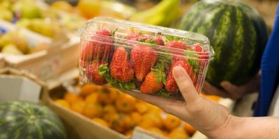 Žena v supermarketu drží plastovou vaničku jahod