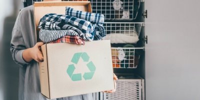 Žena drží v rukou kartonovou krabici s oblečením, koncept recyklace textilu