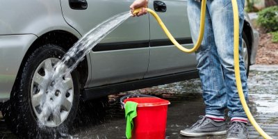 Muž před domem umývá auto hadicí