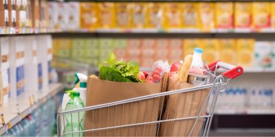 Potraviny a další zboží v papírových taškách v nákupním vozíku v supermarketu