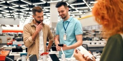 Zákazník a prodavač v prodejně s elektronikou diskutují o mobilním telefonu