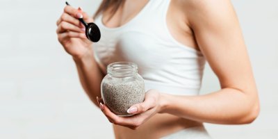 Žena drží v jedné ruce lžičku a v druhé skleničku s šedou náplní