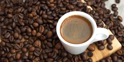 Šálek kávy stojící mezi kávovými boby