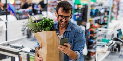 Usmívající se zákazník prochází supermarketem s aplikací v telefonu v ruce