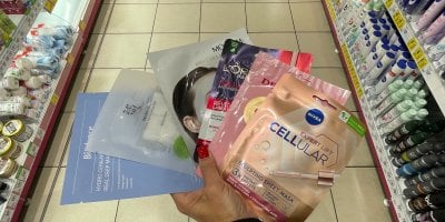 Ženská ruka drží v drogerii plátýnkové masky na obličej v produktových obalech