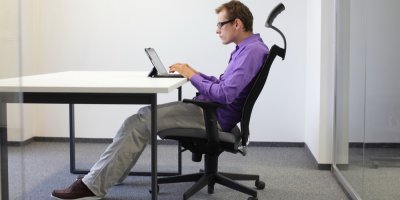 Mladý muž sedí se shrbenými zády na kancelářské židli a pracuje na tabletu
