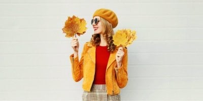 Mladá žena ve stylovém podzimním outfitu drží podzimní listy