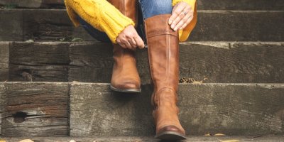 Žena sedící na dřevěných schodech si zapíná kožené kozačky