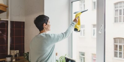 Žena utírá okno v kuchyni stěrkou