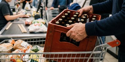 Mužské ruce dávají bednu s pivem do nákupního vozíku v obchodě