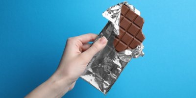 Ženská ruka držící tabulku čokolády na modrém pozadí