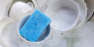 Nádobí a modrá houbička ve vodě se saponátem