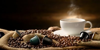 Uvařená káva v bílém hrnku, v popředí kapsle na kávu