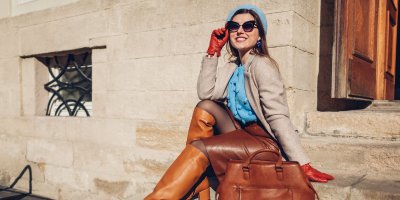 Žena v podzimním outfitu s koženými kozačkami, sakem a modrým svetrem sedí na schodech