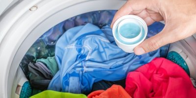 Ruka s pracím gelem a pračka plná barevného prádla