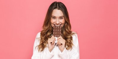 Mladá žena se usmívá a kousá do tabulky čokolády