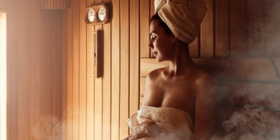 Žena v ručníku leží v sauně, vedle sebe má zapálené svíčky