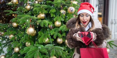Žena v santovské čepici se dívá do prázdné peněženky, v pozadí vánoční stromek