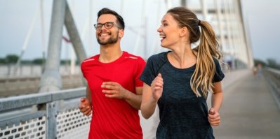 Muž a žena ve sportovním oblečení běhají podél silnice