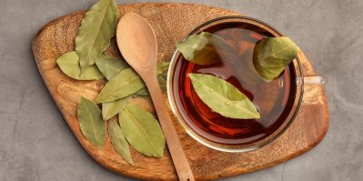 Sklenice s čajem z bobkového listu, ozdobená 3 bobkovými listy, servírovaná na dřevěném prkénku s dřevěnou lžičkou a s několika bobkovými listy