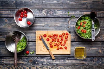 Nakrájená cherry rajčata na prkénku, vedle hrnec s rukolou.