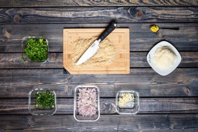 Prkénko s nasekanými oříšky, vedle nakrájená cibule, bylinky.