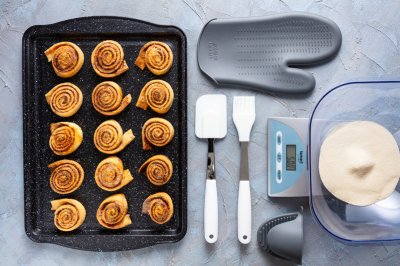 Skořicové šneky na plechu, vedle kuchyňská váha, chňapka a další potřeby