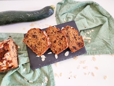 Cuketový chlebíček nakrájený na plátky, v pozadí zbytek chlebíčku a cuketa