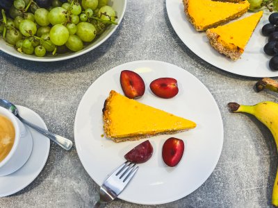 Dýňový cheesecake na bílém talířku, v pozadí miska s hrozny a další kousky cheesecake