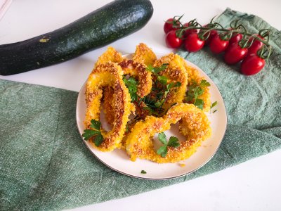 Patizonové řízečky zdobené čerstvou petrželkou, servírované na bílém talíři, v pozadí větvička cherry rajčátek a cuketa