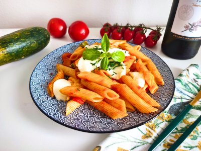 Penne s mozzarellou a rajčaty, zdobené čerstvou bazalkou, servírované na modrém kulatém talíři