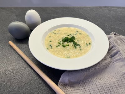 Pórková polévka v bílém talíři posypaná čerstvou pažitkou