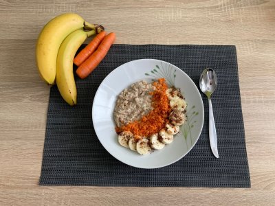 Ovesná kaše, ozdobená mrkví a banánem, servírovaná na bílém talíři