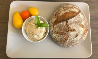 Kváskový chléb na bílém tácku, vedle pomazánka v misce a rajčata