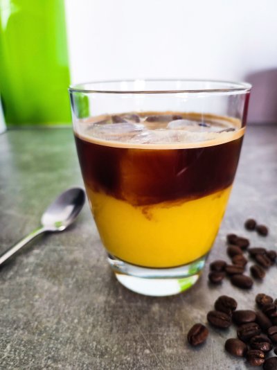 Espresso orange na šedé pracovní desce, vedle kávová zrna a lžička