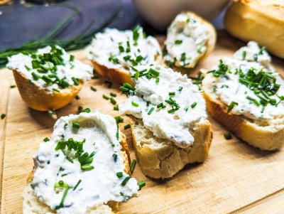 Česnekovo-pažitková pomazánka na kouscích bagety ležících na dřevěném prkénku