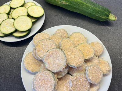 Obalená cuketa nachystaná na smažení, v pozadí cuketa nakrájená na plátky