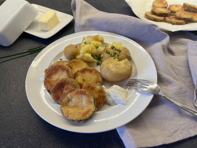 Smažená cuketa s novými brambory uvařenými ve slupce, v pozadí máslo